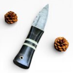 Handcrafted knife with a black handle and silver blade, surrounded by pine cones on a white background.